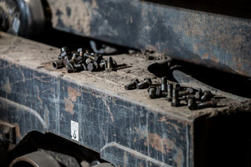 Collection of steel bolts lying on old machine part covered in dirt representing mechanical repair, industrial work environment, and construction maintenance