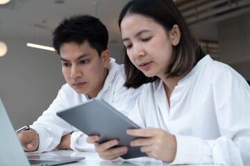 Man and woman analyzing information with laptop and tablet in modern office, representing teamwork,...
