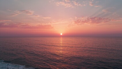 Obraz premium Shining sun casting hues across rippling ocean at sunset under pink purple sky and scattered clouds