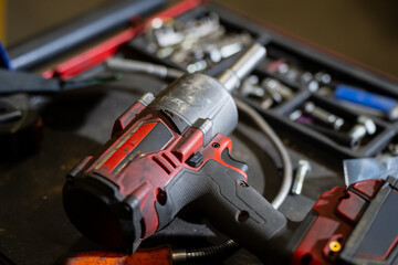 Professional cordless impact wrench with red and black housing resting on mechanic workbench with assorted sockets and automotive repair tools