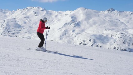 Person fast skiing down groomed slope against snow covered mountain range at ski resort. Active winter sports on vacation. Shot side view, in motion following near skier. Female skier turning slalom - Powered by Adobe
