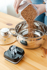 Woman's hands pour buckwheat groats from a transparent container into a saucepan