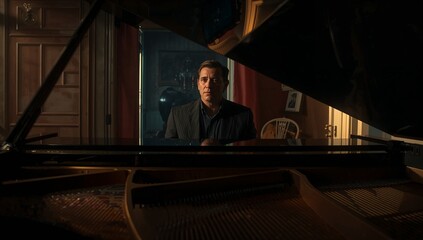Man in suit playing grand piano in music room, with open lid showing strings and globe