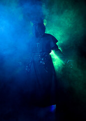 Plague Doctor Halloween Costume Portrait with Glowing Green Misty Fog, Gothic Character in Black Cloak bird Mask, Dark Fantasy Horror Scene with silhouette figure Spooky Atmospheric Lighting.