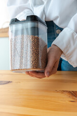 Filled buckwheat plastic containers with woman hands on the kitchen background