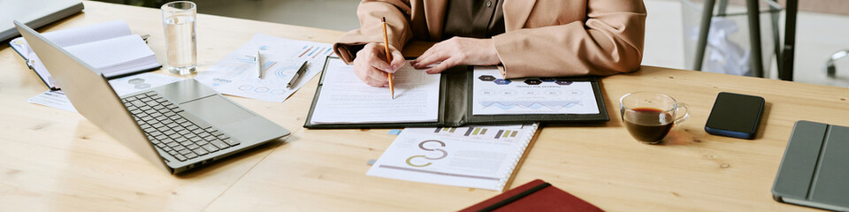 Middle aged Caucasian woman working at desk, reviewing documents and writing notes, surrounded by...