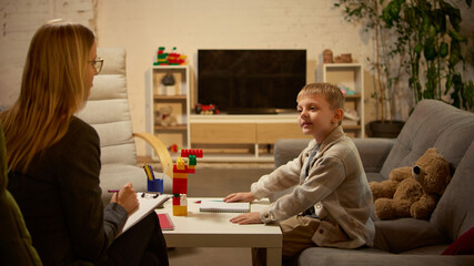 Smiling boy showing colorful toy blocks to psychologist during developmental therapy. Concept of emotional intelligence, play-based learning, educational psychology for family counseling and awareness