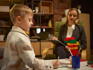 Boy drawing and playing with psychologist during emotional development session. Concept of learning through creativity, healthcare psychology, educational materials for therapy and child growth.