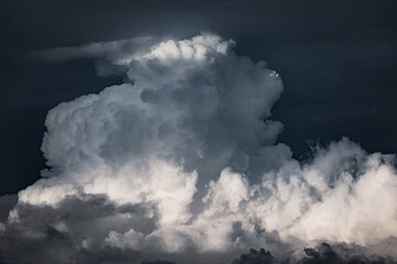 Large cumulonimbus cloud building in a dark sky. Sunlight illuminating parts of the cloud while others remain deep in shadow