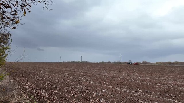 Large machines work the soil in the fall. Tractors till the land while it is raining.
The weather is bad.