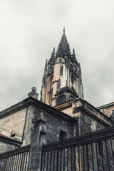 Gothic cathedral tower in Oviedo, Asturias, Spain, rising dramatically against a cloudy sky, showcasing intricate stone architecture, historical details, and medieval atmosphere in moody lighting