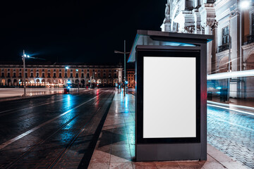Night city scene with illuminated blank billboard mockup at a modern bus stop, wet pavement reflecting neon lights and passing traffic, perfect for urban advertising or branding presentation