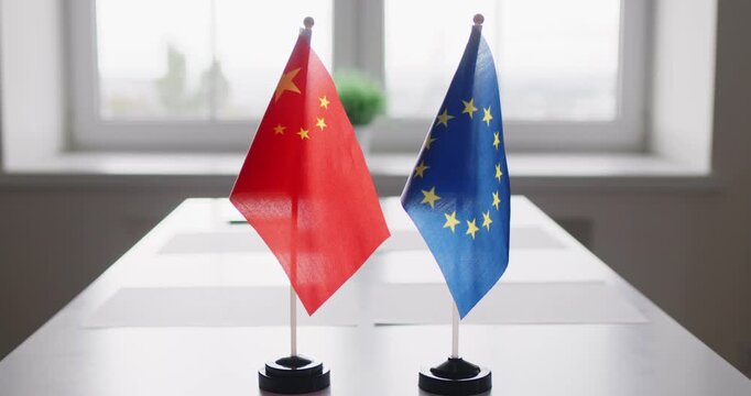 Flags signal diplomacy and negotiation between EU, China. Two desktop flags on a conference table, indicating formal meeting dialogue. Symbolizes bilateral diplomatic trade negotiations.