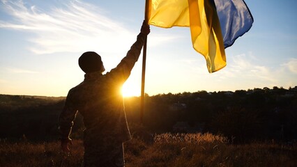 Young soldier of ukrainian army lifted blue-yellow banner in honor of the victory against russian...