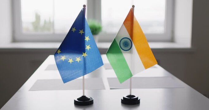 Flags signal diplomacy and negotiation between EU, India. Two desktop flags on a conference table, indicating formal meeting dialogue. Symbolizes bilateral diplomatic trade negotiations.