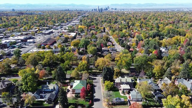 Washington Virginia Vale neighborhood in Denver during peak fall, showing vibrant colorful tree canopy, two-story homes, flat-roof retailers, and Colorado Boulevard leading to skyline, mountains