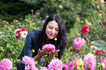 Midlife woman enjoying vibrant flowers in a lush garden, surrounded by colorful blooms, embracing...