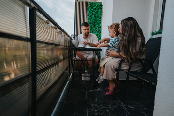 Obraz premium A family spends a relaxed afternoon on a balcony, sharing a meal at a small table. The parents cradle their child as they converse, creating a warm, together moment in a contemporary outdoor space.