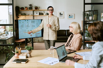 Caucasian middle aged woman presenting data on digital screen to two middle aged Caucasian women...