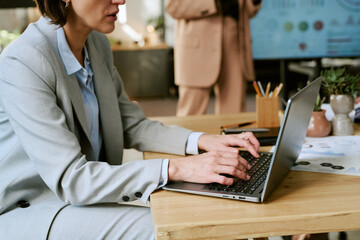 Caucasian middle aged woman working on laptop at desk in modern office, hands typing on keyboard,...