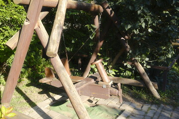 Custom-made, wooden airplane swing set stands outdoors with green foliage behind it.
