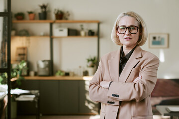 Portrait of middle aged Caucasian woman with blond hair and glasses standing with arms crossed in...