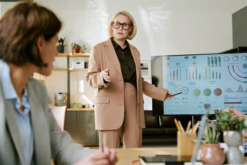 Caucasian middle-aged woman presenting business data on digital screen during meeting, gesturing...