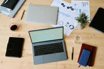 Overhead view showing open laptop, smartphone, notebooks, coffee cup, glass of water, pen, potted...