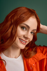 Fototapeta premium Redhead woman showcases autumn fashion in vibrant orange attire against green backdrop