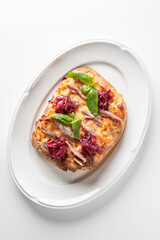 A mini pizza or flatbread with anchovies, caramelized red onions, cheese, and fresh basil leaves on an oval white plate with a neutral background