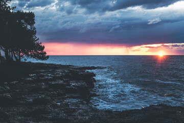 sunset over the sea in istria, croatia, with waves, dramatic purple clouds and the sun right on the horizon