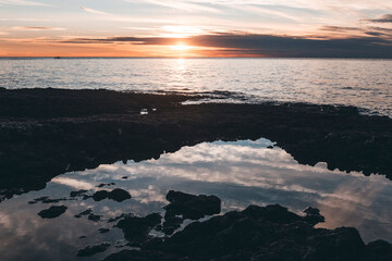sunset from the cape in croatia, with reflections on the water and rocks foreground