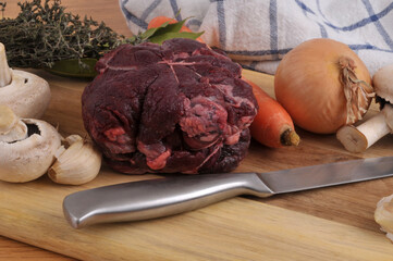 Joue de boeuf crue sur une planche à découper avec un couteaau et des ingrédients en gros plan