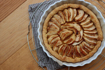 Traditional french cake Tart aux pommes with sliced apples on a cooling rack on wooden table