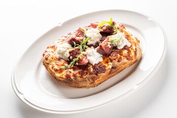 A close-up shot of a gourmet toast topped with melted cheese, fresh figs, creamy ricotta, and greens on a white plate, ready to be served.