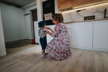 A mother kneels in a floral dress, sharing a drink with her child in a sunlit, modern kitchen. The...