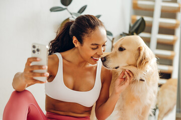 Portrait of happy African American woman holding mobile phone petting golden retriever taking selfie