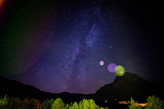 Breathtaking night sky panorama showcases the Milky Way galaxy over silhouetted mountains and vibrant trees, inspiring wonder and awe.