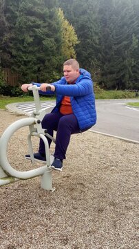 Overweight young man exercising on fitness machine outdoor