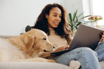 Candid African American woman businesswoman using working on laptop petting golden retriever