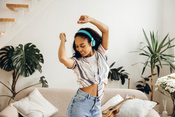 Positive, smiling authentic woman listening music in earphones enjoying in living room at home