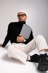 Stylish young man poses confidently with laptop in modern studio setting