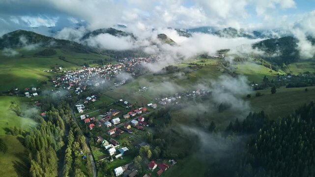 Aerial hyperlapse of mountain village with drifting fog and morning sunlight over green valley