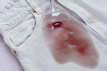 Spilled glass with red wine falled a top a light blue pair of jeans, while a noticeable red stain...