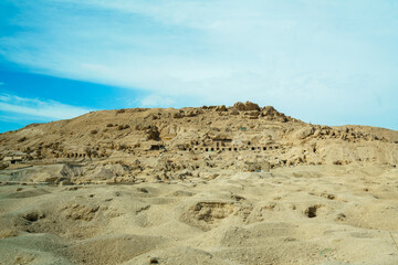 Wide angle shot of a desert cliff face with numerous ancient tombs or dwellings carved into the rock along the road to Colossi of Memnon Luxor Egypt.