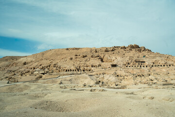 Desert landscape with ancient rock-cut tombs and archaeological ruins along the road from Valley of the Kings to Colossi of Memnon in Luxor, Egypt. 2025.