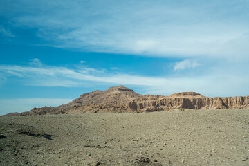 Wide angle shot of a desert cliff face with numerous ancient tombs or dwellings carved into the rock along the road to Colossi of Memnon Luxor Egypt.