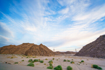 Wide angle view of the dramatic desert mountains and sparse vegetation under a wispy blue sky on the long road trip from Luxor to the Red Sea resort of Hurghada Egypt.