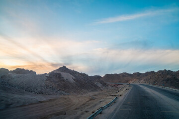 Dusk highway view to Hurghada Red Sea Resort, Egypt, with rugged hills and dreamy clouds, captured in spring 2025 during a bus journey, showcasing a serene landscape.