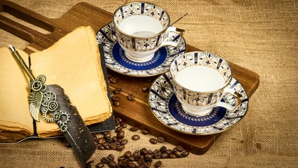 Fotobehang Koffiebar A beautifully composed still-life photograph featuring two blue and gold patterned tea cups alongside a vintage feather quill, aged paper, and coffee beans. Ideal for hospitality, lifestyle, food  © Vivek